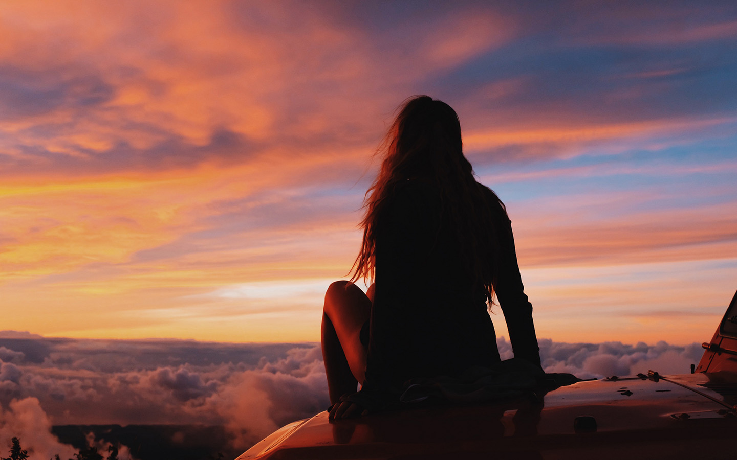 Josette Munoz sitting on hood of car looking at sunset
